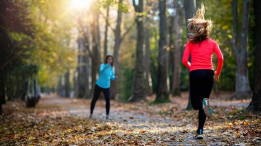 Kamu Parkında Kadın Egzersizi Sonbaharda Kişisel Eğitmenle. Eğitmen Amigoluk ve Koşan Kadın.
