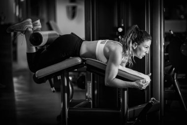 Spor salonundaki kıvrımlı bankta egzersiz yapan kadın sporcu, siyah ve beyaz.