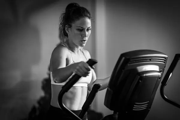 Woman exercising on cycling machine or exercise bike, black and white