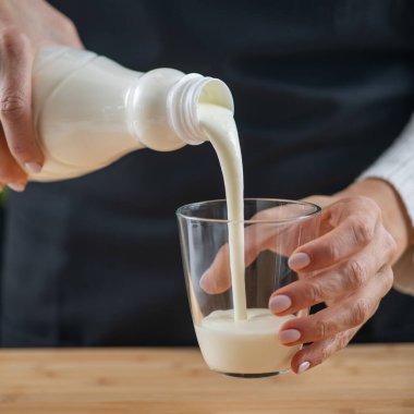woman pouring kefir, a fermented dairy superfood drink, brimming with natural probiotics Lacto and Bifido Bacterium. clipart