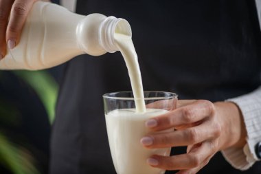 woman pouring kefir into the glass, a fermented dairy superfood drink, brimming with natural probiotics Lacto and Bifido Bacterium. clipart