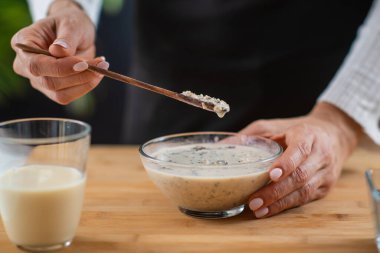 Yulaf, soya sütü ve bitki protein tozu içeren yulaf ezmesi hazırlayan kadın, sağlık ve lezzetin kaynaşmasını gösteriyor.