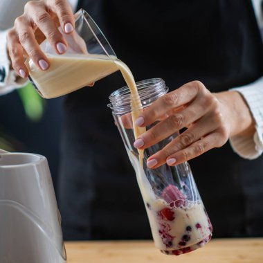 Lezzetli bir sağlık hizmeti için soya sütü ve canlı böğürtlenlerle besleyici bir karışım hazırlayan kadın. 