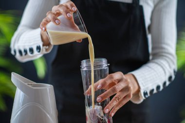 Lezzetli bir sağlık hizmeti için soya sütü ve canlı böğürtlenlerle besleyici bir karışım hazırlayan kadın. 