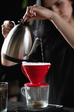 Kadın barista kahve yapıyor, kahve telvesine sıcak su döküyor.