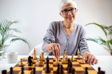 Senior woman playing chess at home clipart