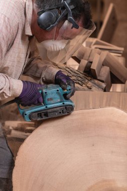 Marangoz mobilya fabrikasında zımpara makinesi kullanarak dev bir tahta parçasını parlatıyor.
