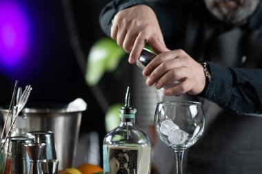 Yetenekli bir barmen, boş bir bardağa buz koyup kokteyl hazırlıyor.