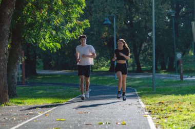 Canlı bir parkta koşuşturan, spor yapmayı kucaklayan ve aktif bir yaşam tarzı olan çift. Bu fotoğraf açık hava egzersizini, sağlığını ve doğada koşmanın keyfini vurgular..