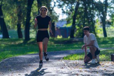 Parkta koşan bir çift aktif bir yaşam tarzını ve form düzenini benimsiyor. Görüntü, sağlık, enerji ve doğal ve huzurlu bir ortamda birlikte egzersiz yapmanın neşesini vurgular.