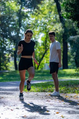 Canlı bir parkta koşuşturan, spor yapmayı kucaklayan ve aktif bir yaşam tarzı olan çift. Bu fotoğraf açık hava egzersizini, sağlığını ve doğada koşmanın keyfini vurgular..