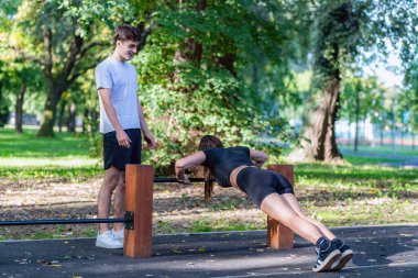 Parkta açık hava ekipmanları üzerinde egzersiz yapan çift sağlıklı ve aktif bir yaşam tarzının tadını çıkarıyor. Dekor, takım çalışmasını, spor yapmayı ve doğal bir ortamda dışarıda çalışmanın faydalarını vurgular..