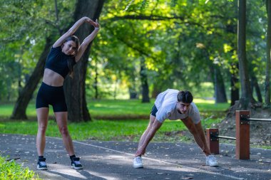 Çift parkta birlikte egzersiz yapıyor, fitness ve sağlıklı bir yaşam tarzını destekliyor. Serin açık hava ortamında bağlılık, fiziksel aktivite ve doğanın ortasında olmak vurgulanıyor..