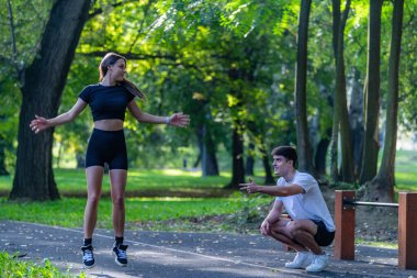 Çift parkta birlikte egzersiz yapıyor, fitness ve sağlıklı bir yaşam tarzını destekliyor. Serin açık hava ortamında bağlılık, fiziksel aktivite ve doğanın ortasında olmak vurgulanıyor..