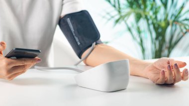 Bir kadın kan basıncını ölçer, kan basıncını ölçerken akıllı telefona veri girerken sağlık hizmetine modern bir yaklaşım gösterir.