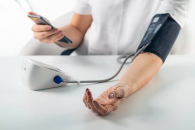 Bir kadın kan basıncını ölçer. Kan basıncı ölçülürken modern bir sağlık yaklaşımı ve kullanışlı izleme için akıllı telefondan veri girişi