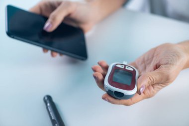 Bir kadın, diyabet yönetimi ve sağlık izleme için hayati önem taşıyan glikoz seviyelerini takip eder ve akıllı telefondan veri girişi yapar