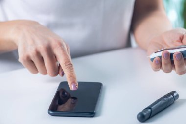 Bir kadın glikoz seviyelerini takip eder ve akıllı telefondan veri girer, diyabet yönetimi ve izleme için hayati önem taşır