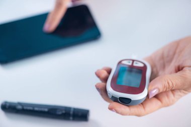 Glikoz seviyelerini ölçen bir kişi, diyabet yönetimi için gerekli olan sonuçları izlemek ve analiz etmek için akıllı telefon uygulaması kullanır.