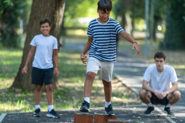 İki çocuk dışarıda spor faaliyetlerine katılıyor, bir antrenörün rehberliğinde tahta kütükler arasında denge kuruyorlar. Doğal ortam, bu eğlenceli egzersiz sırasında koordinasyonu ve odaklanmayı teşvik eder..