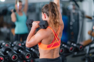 Çağdaş bir spor salonunda ağırlık kaldıran bayan sporcu fitness ve arkadaşlığı teşvik ediyor.