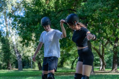 Genç çift manzaralı bir parkta birlikte paten kaymaktan hoşlanıyor. Çift yol boyunca süzülüyor, yeşilliklerle çevrili, sağlıklı kalırken eğlenceli ve aktif bir açık hava deneyimi paylaşıyor..