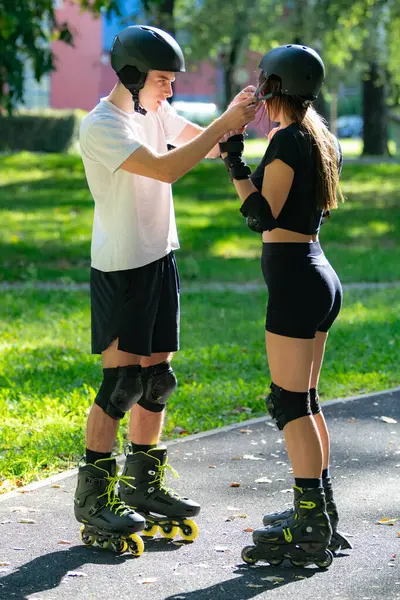 Adam kadının kaskına yardım ederken çift paten kaymaya hazırlanıyor. Bir anlık bakım ve takım çalışmasını paylaşıyorlar. Açık hava aktivitelerinin keyfini çıkarmadan önce güvenliği sağlıyorlar..