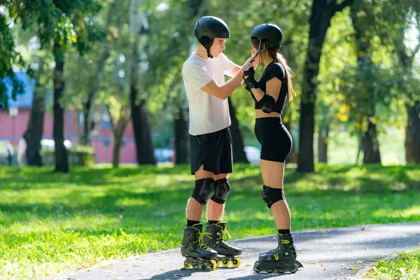 Adam kadının kaskına yardım ederken çift paten kaymaya hazırlanıyor. Bir anlık bakım ve takım çalışmasını paylaşıyorlar. Açık hava aktivitelerinin keyfini çıkarmadan önce güvenliği sağlıyorlar..