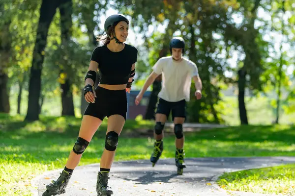 Genç çift, güneşli bir yaz gününde yemyeşil bir parkta paten kaymaktan hoşlanıyor. Çift, etkin bir yaşam tarzını kucaklayarak ve keyifli bir açık hava deneyimini paylaşarak manzaralı yollarda süzülür..