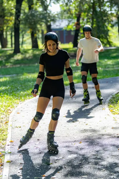 Genç çift, güneşli bir yaz gününde yemyeşil bir parkta paten kaymaktan hoşlanıyor. Çift, etkin bir yaşam tarzını kucaklayarak ve keyifli bir açık hava deneyimini paylaşarak manzaralı yollarda süzülür..