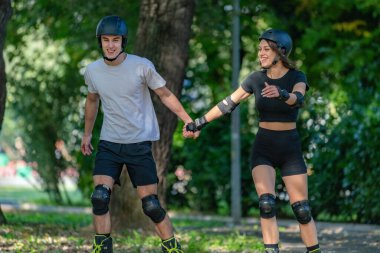 Genç çift, güneşli bir yaz gününde yemyeşil bir parkta paten kaymaktan hoşlanıyor. Çift, etkin bir yaşam tarzını kucaklayarak, manzaralı patikalarda süzülür.