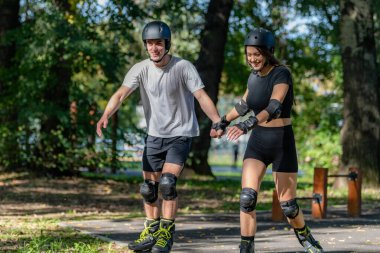 Genç çift, güneşli bir yaz gününde yemyeşil bir parkta paten kaymaktan hoşlanıyor. Çift, etkin bir yaşam tarzını kucaklayarak, manzaralı patikalarda süzülür.