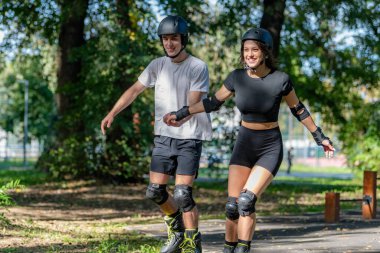 Genç çift, güneşli bir yaz gününde yemyeşil bir parkta paten kaymaktan hoşlanıyor. Çift, etkin bir yaşam tarzını kucaklayarak, manzaralı patikalarda süzülür.