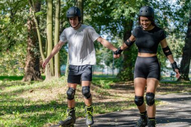 Genç çift, güneşli bir yaz gününde yemyeşil bir parkta paten kaymaktan hoşlanıyor. Çift, etkin bir yaşam tarzını kucaklayarak, manzaralı patikalarda süzülür.