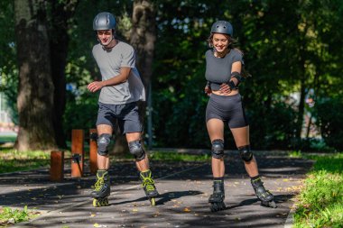 Genç çift, güneşli bir yaz gününde yemyeşil bir parkta paten kaymaktan hoşlanıyor. Çift, etkin bir yaşam tarzını kucaklayarak, manzaralı patikalarda süzülür.