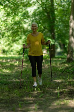 Aktif olgun bir kadın, doğası gereği güzel olan İskandinav yürüyüş egzersizi yapar..