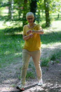 Kıdemli kadın spor ve sağlık için parkta yürürken akıllı adımları takip ediyor..