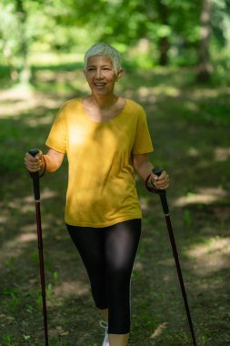 Aktif olgun bir kadın, doğası gereği güzel olan İskandinav yürüyüş egzersizi yapar..