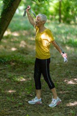 Kıdemli kadın parkta etkili bir egzersiz yapmak için direniş bandıyla antrenman yapıyor..