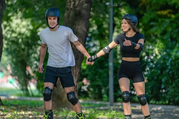 Genç çift, güneşli bir yaz gününde yemyeşil bir parkta paten kaymaktan hoşlanıyor. Çift, etkin bir yaşam tarzını kucaklayarak, manzaralı patikalarda süzülür.