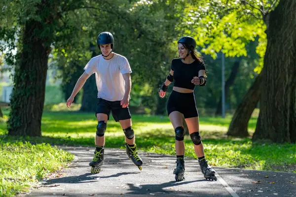 Genç çift, güneşli bir yaz gününde yemyeşil bir parkta paten kaymaktan hoşlanıyor. Çift, etkin bir yaşam tarzını kucaklayarak, manzaralı patikalarda süzülür.