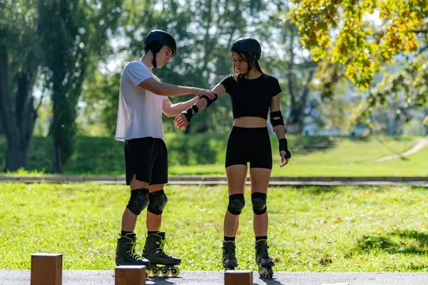 Çift paten kaymaya hazırlanırken erkek, kadının koruyucu kol bantlarını güvene almasına yardım ediyor. Bir anlık bakım ve takım çalışmasını paylaşıyorlar. Açık hava aktivitelerinin keyfini çıkarmadan önce güvenliği sağlıyorlar..