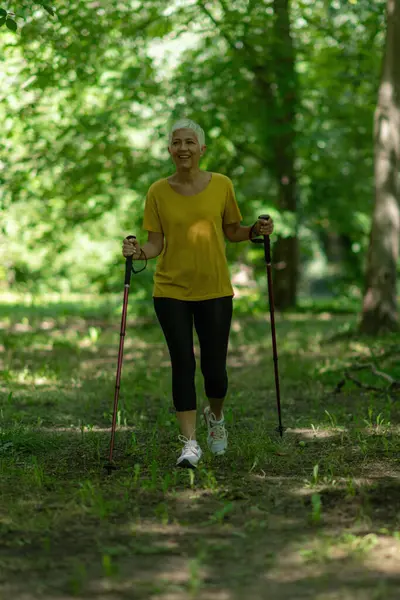Aktif olgun bir kadın, doğası gereği güzel olan İskandinav yürüyüş egzersizi yapar..