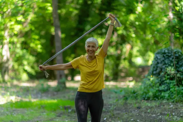 Parkta etkili egzersiz yapmak için direniş bandıyla egzersiz yapan yaşlı bir kadın..