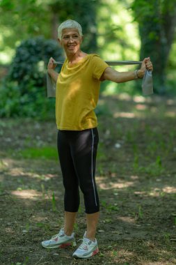 Doğada elastik direniş bandıyla egzersiz yapan aktif kıdemli kadın.. 
