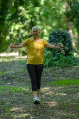Doğadaki dayanıklılık eğitimi için elastik direniş bandıyla egzersiz yapan aktif kıdemli kadın..
