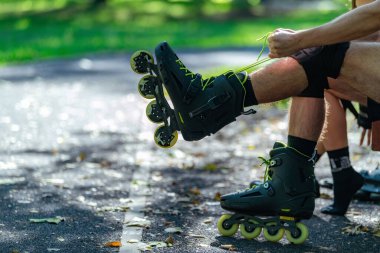 Adam dışarıda patenli bir maceraya hazırlanıyor, patenlerini manzaralı bir parkta takıyor..