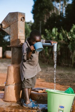 Kitale, Kenya - 02.03.2017: Evsiz çocuklara yardım etmek için hayır kurumundan bir misyoner ekibi geldi. Yiyecek, giyecek ve su paylaşıyorlar. Afrika 'da açlık ve işsizlik. Küçük bir çocuk kuyudan su içiyor. Afrika 'da su sıkıntısı.