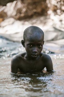 Kitale, Kenya - 02.03.2017: Evsiz çocuklara yardım etmek için hayır kurumundan bir misyoner ekibi geldi. Yiyecek, giyecek ve su paylaşıyorlar. Afrika 'da açlık ve işsizlik. Nehirde yüzen bir çocuğun portresi.