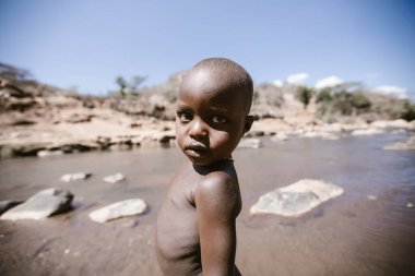 Kitale, Kenya - 02.03.2017: Evsiz çocuklara yardım etmek için hayır kurumundan bir misyoner ekibi geldi. Yiyecek, giyecek ve su paylaşıyorlar. Afrika 'da açlık ve işsizlik. Nehirde yüzen bir çocuğun portresi.
